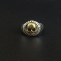 Gold and silver ring with skull design on a black background