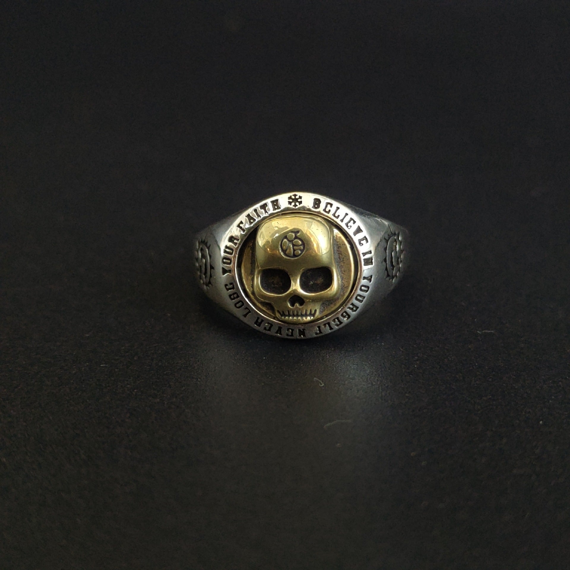 Gold and silver ring with skull design on a black background
