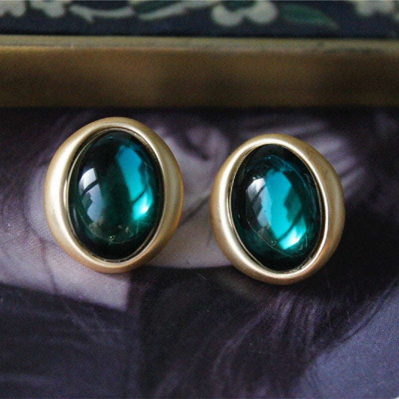 Gold earrings with green gemstones on a dark fabric background