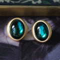 Gold earrings with green gemstones on a dark fabric background