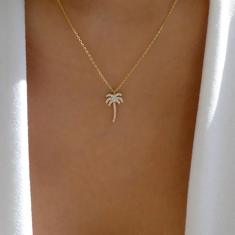 Gold necklace with a palm tree pendant on a person's neck against a white background