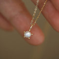 Delicate gold necklace with a pearl pendant held between fingers against a blurred background