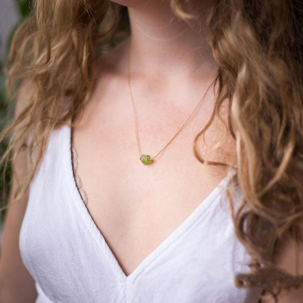 Woman wearing a white top and a necklace with a green pendant.