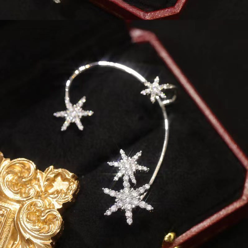 Silver star-shaped earrings on a dark surface with a gold object partially visible.