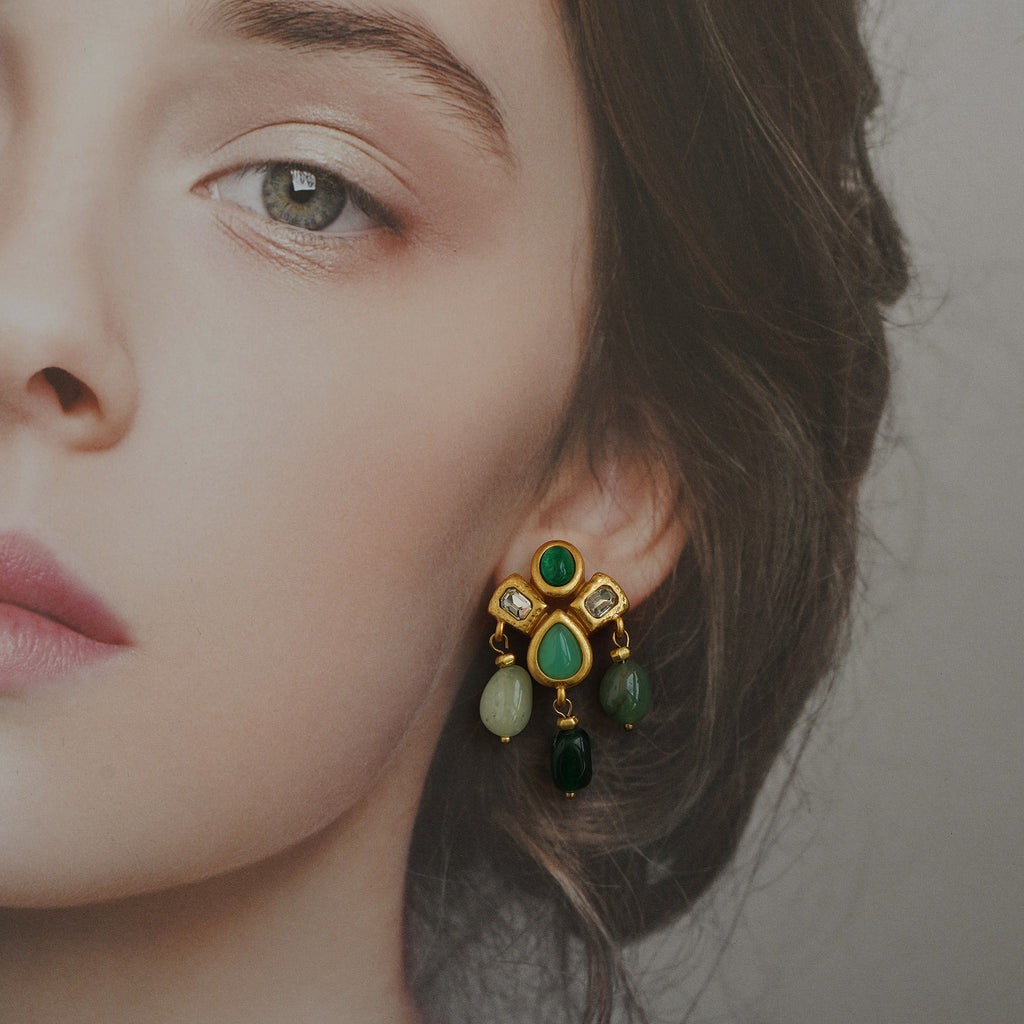 Close-up of a woman wearing a gold earring with green gemstones.