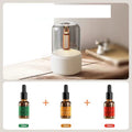 White diffuser with a glass cover on a wooden surface, accompanied by three dropper bottles of different sizes.