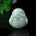 Green jade Buddha pendant on a reflective surface with a blurred green leaf background