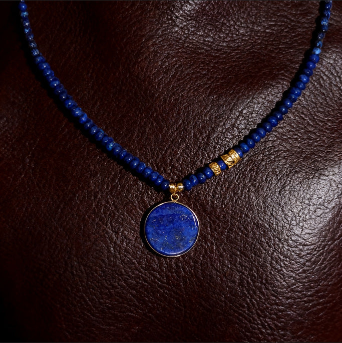 Blue beaded necklace with a round blue pendant on a brown leather surface