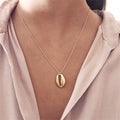 Gold necklace with a pendant worn by a person wearing a light pink shirt.