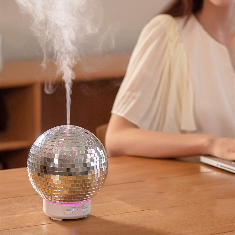 Silver disco ball humidifier on a wooden table with a person sitting in the background.
