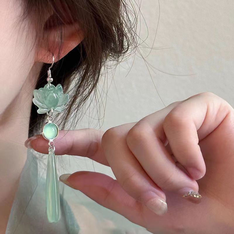 Close-up of a hand wearing a green floral earring with a tassel.