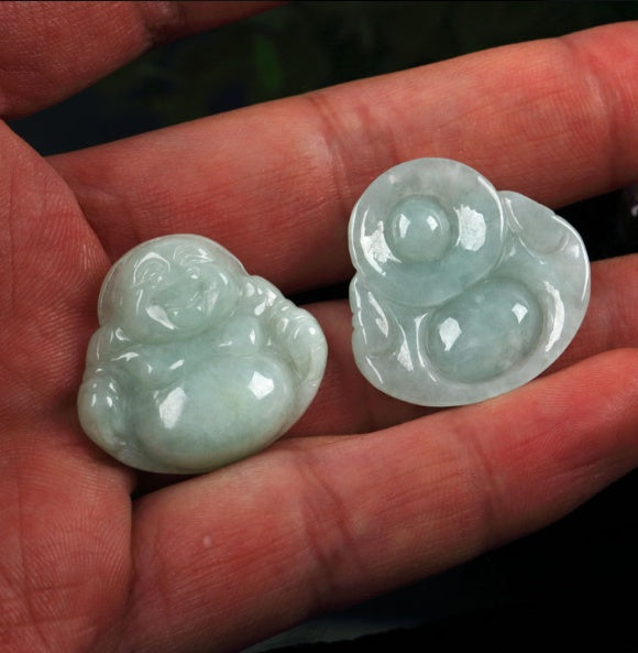 Two jade Buddha pendants held in a hand.