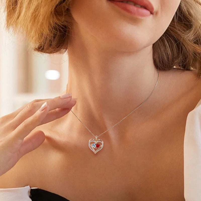 Woman wearing a silver necklace with a heart-shaped pendant featuring a red gemstone.