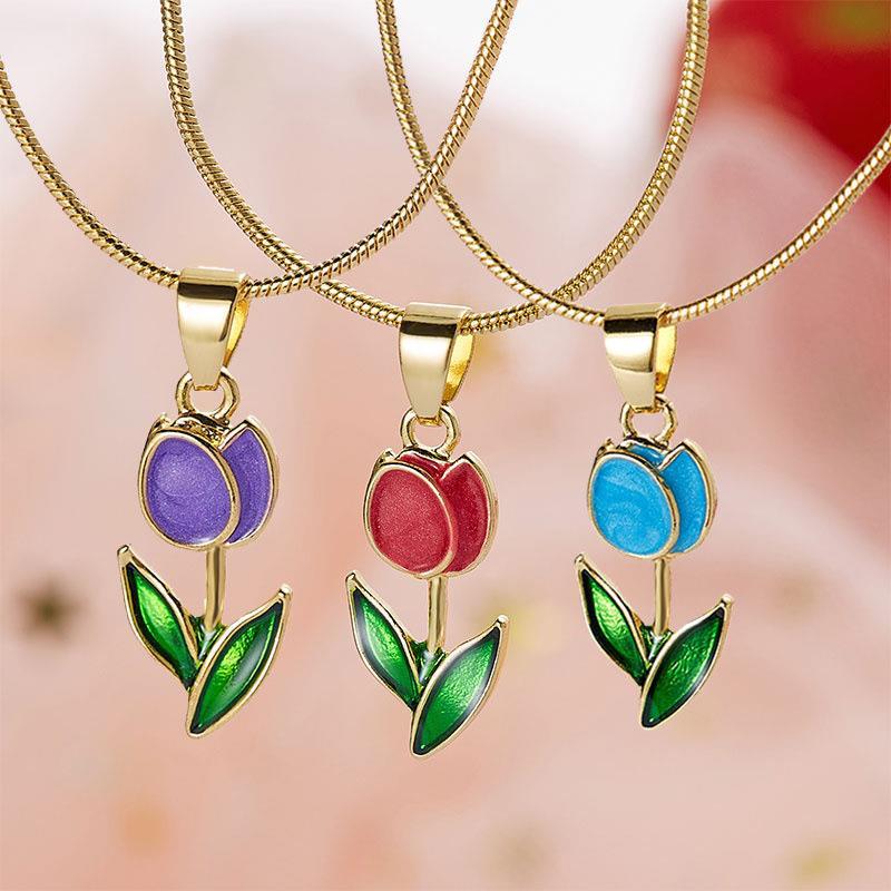 Three colorful tulip pendants on gold chains against a blurred background