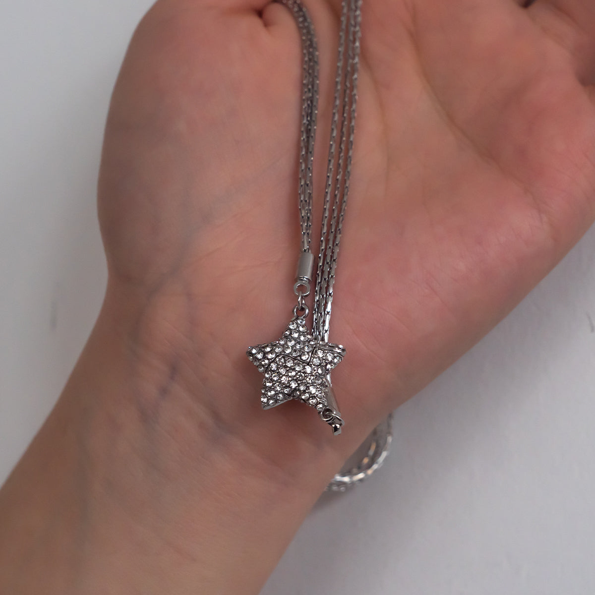Silver star-shaped pendant on a chain held in a hand against a neutral background