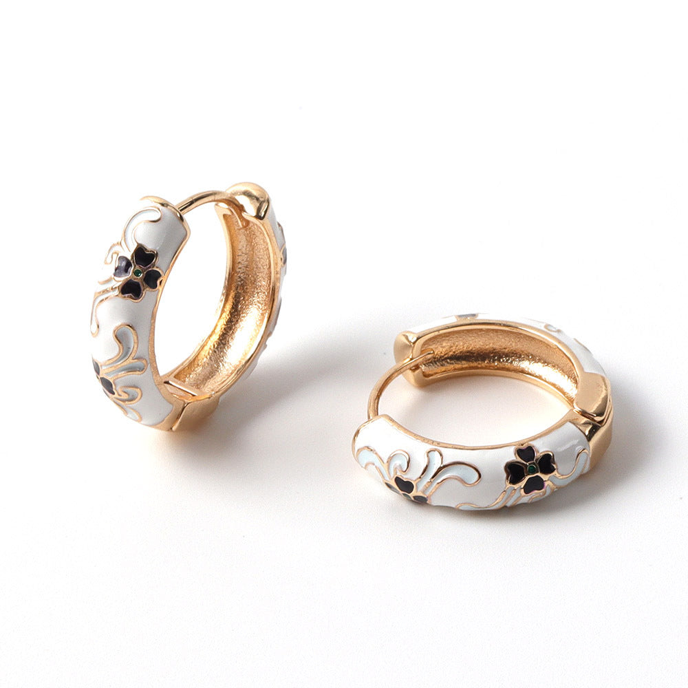 Pair of gold and white hoop earrings with floral designs on a white background
