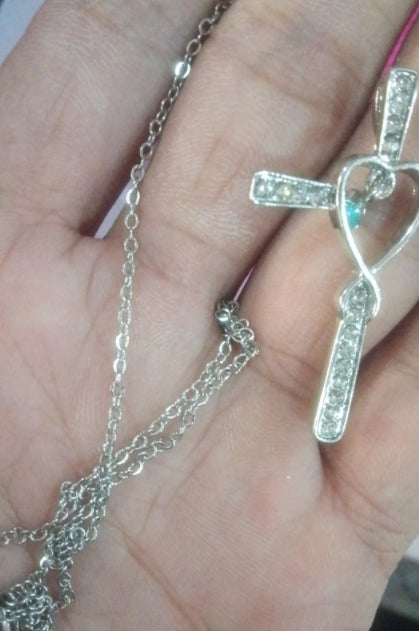 Silver necklace with a cross pendant held in a hand.