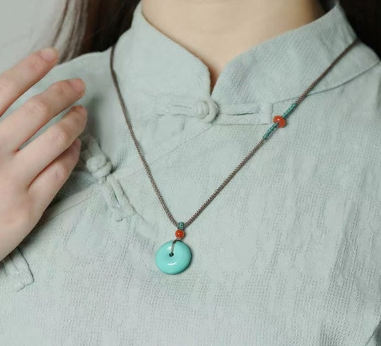 Person wearing a light blue shirt with a necklace featuring a turquoise pendant.