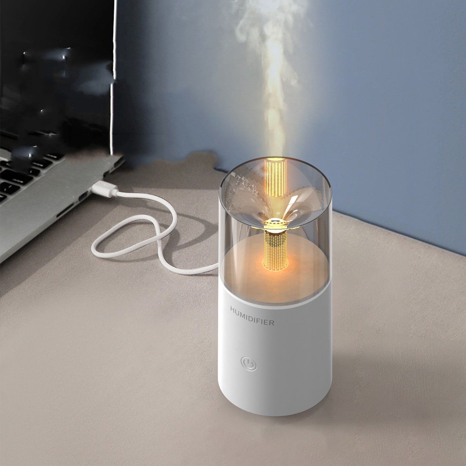 Small humidifier emitting mist on a desk next to a laptop.