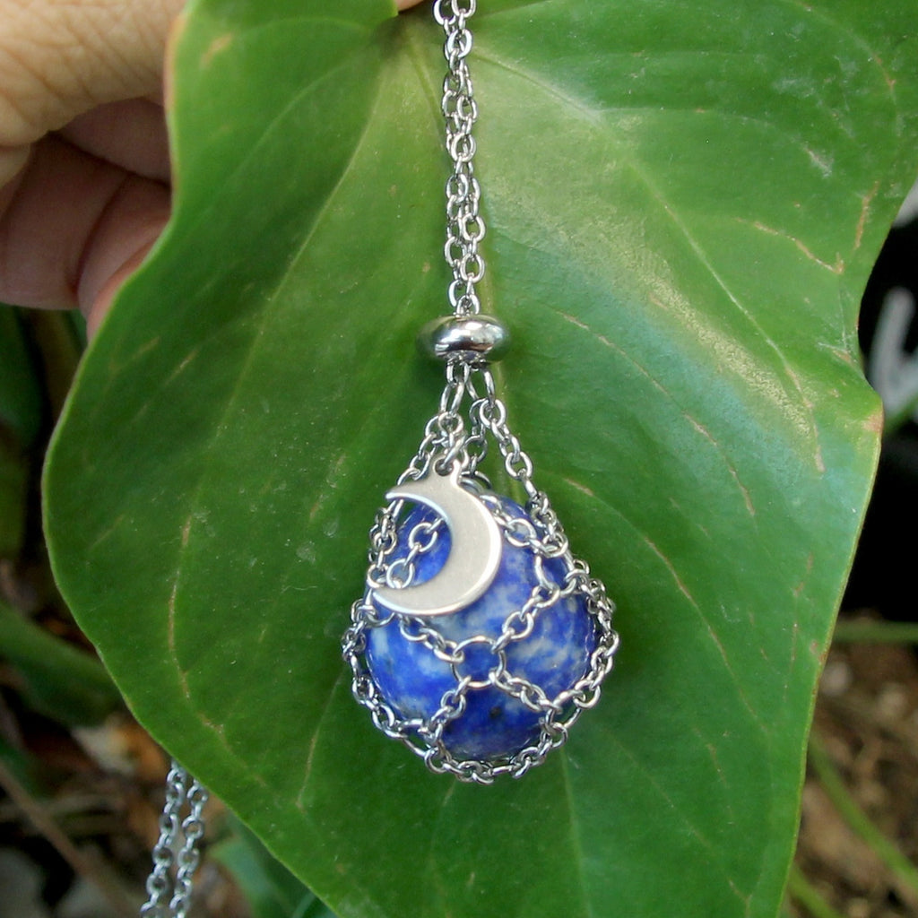 Blue and silver pendant with moon design on a green leaf