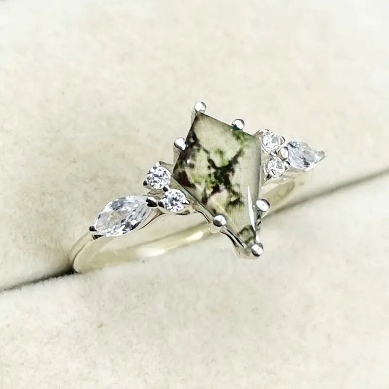 Silver ring with a large green stone and smaller clear stones on a beige background