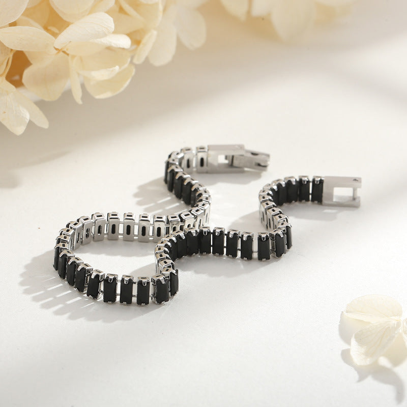 Silver bracelet with black stones on a light surface with flowers in the background