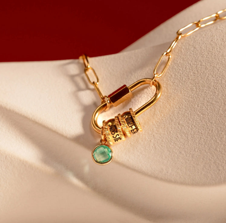 Gold padlock charm with a green gemstone on a beige surface
