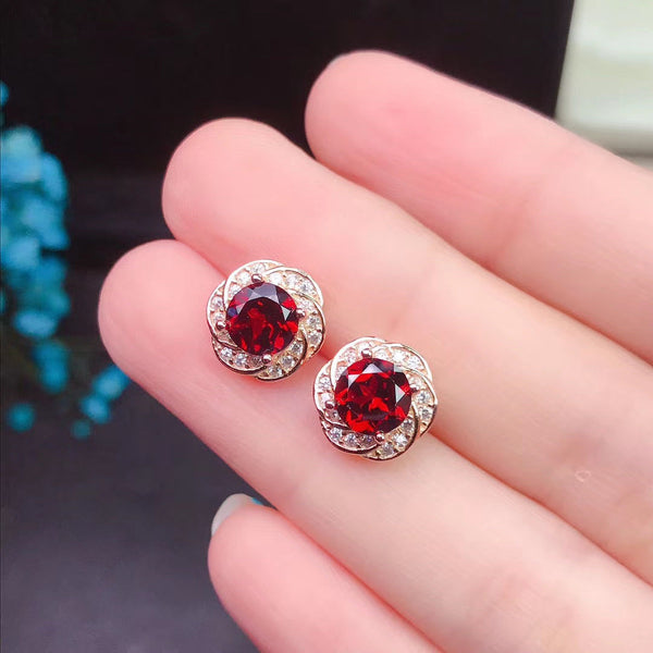 Red gemstone earrings held between fingers against a dark background