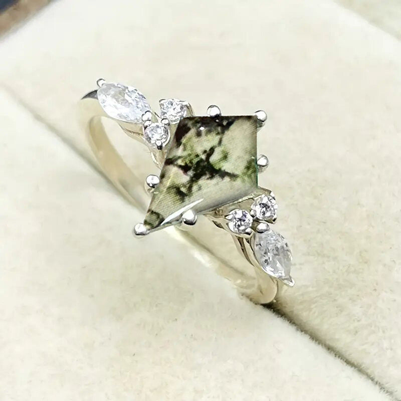 Silver ring with a green gemstone and diamond accents on a beige background