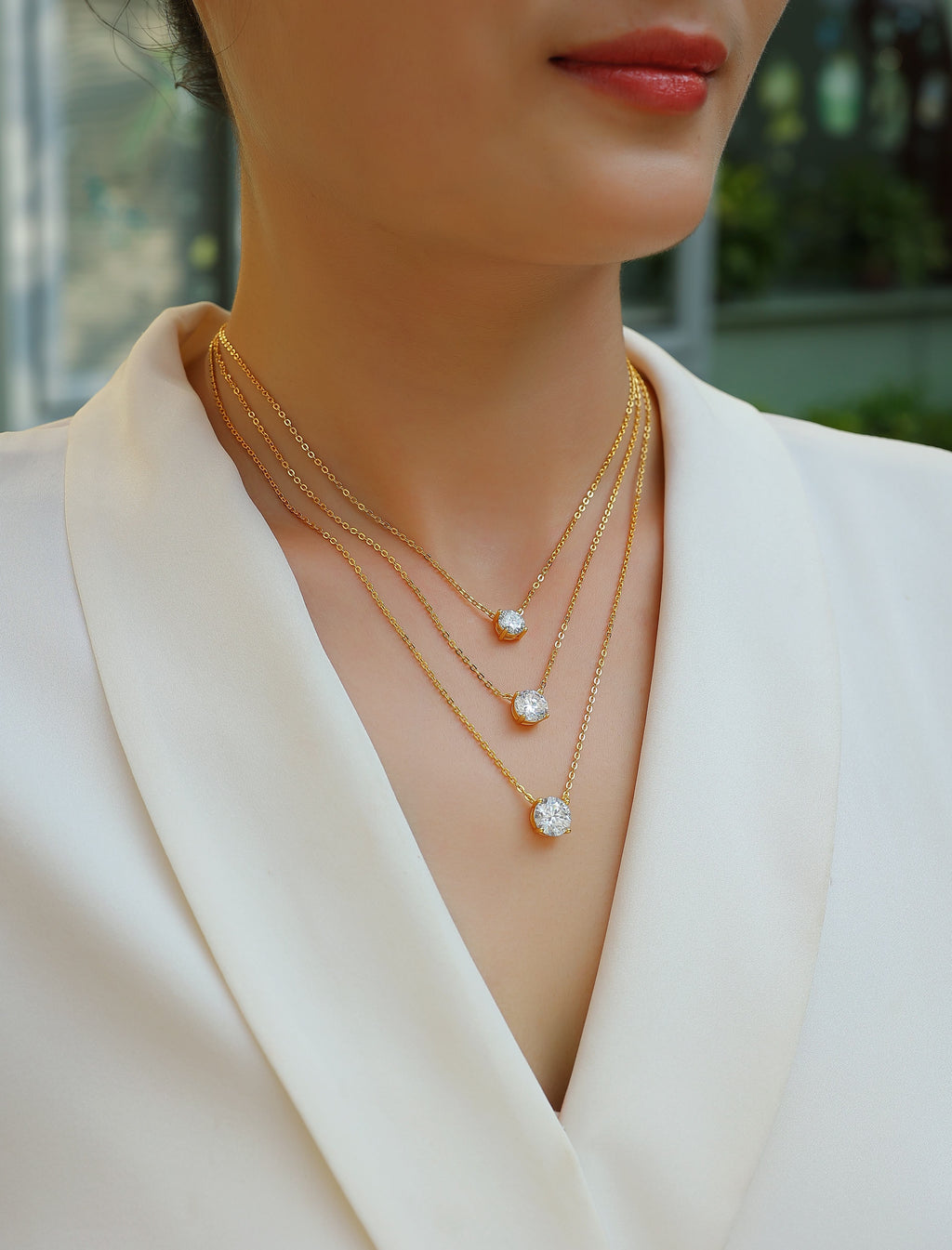 Close-up of a person wearing a delicate gold necklace with small pendants against a blurred outdoor background.