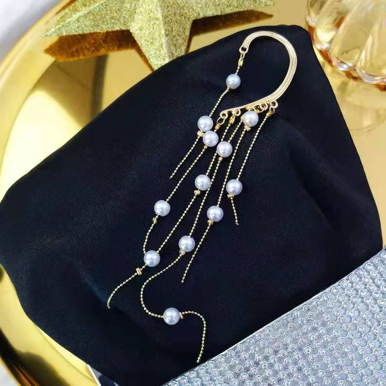 Pearl earring on a black fabric with a gold star and glass bottle in the background