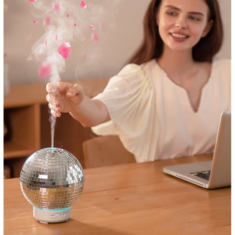 Person using a disco ball humidifier on a desk with a laptop in the background