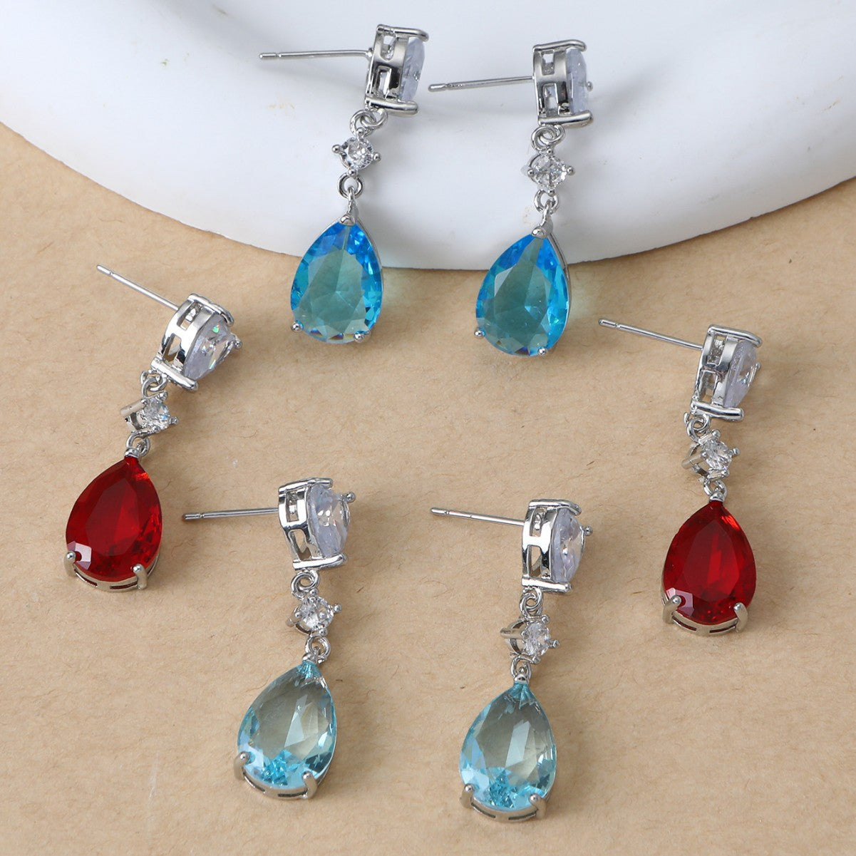 Pair of earrings with blue and red teardrop-shaped gemstones on a beige surface.