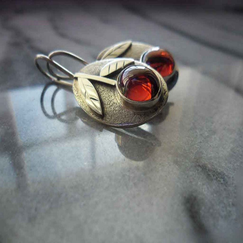 Silver earrings with red gemstones on a gray surface