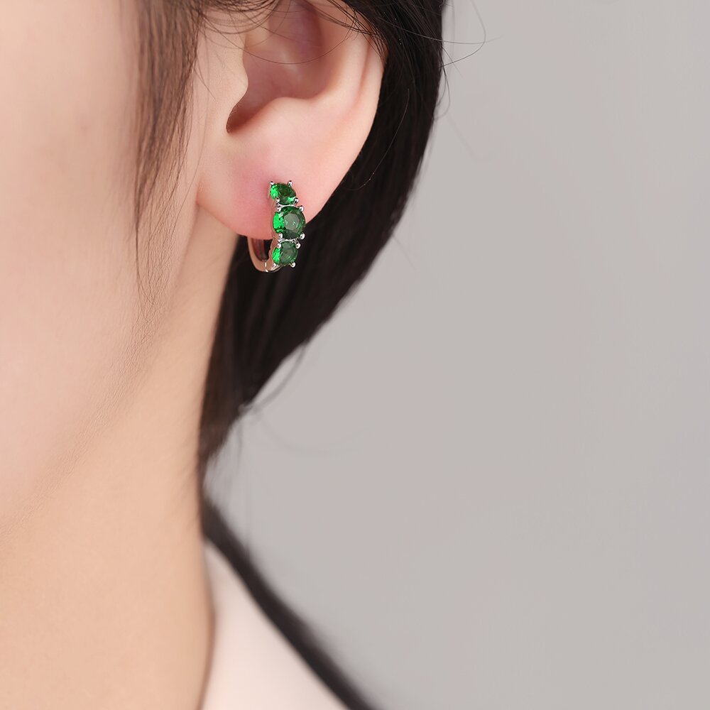 Close-up of an ear wearing a green gemstone earring with a neutral background