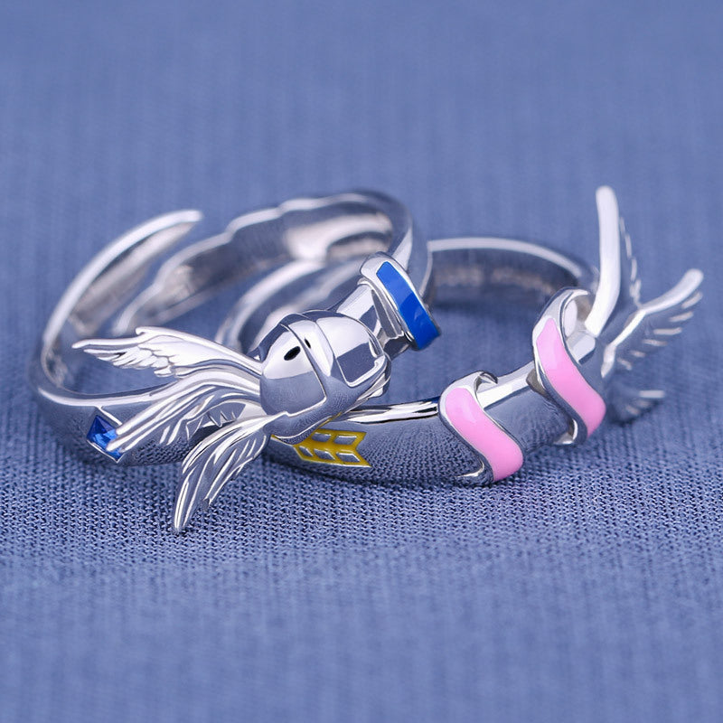 Silver ring with angel wings and colorful accents on a blue fabric background