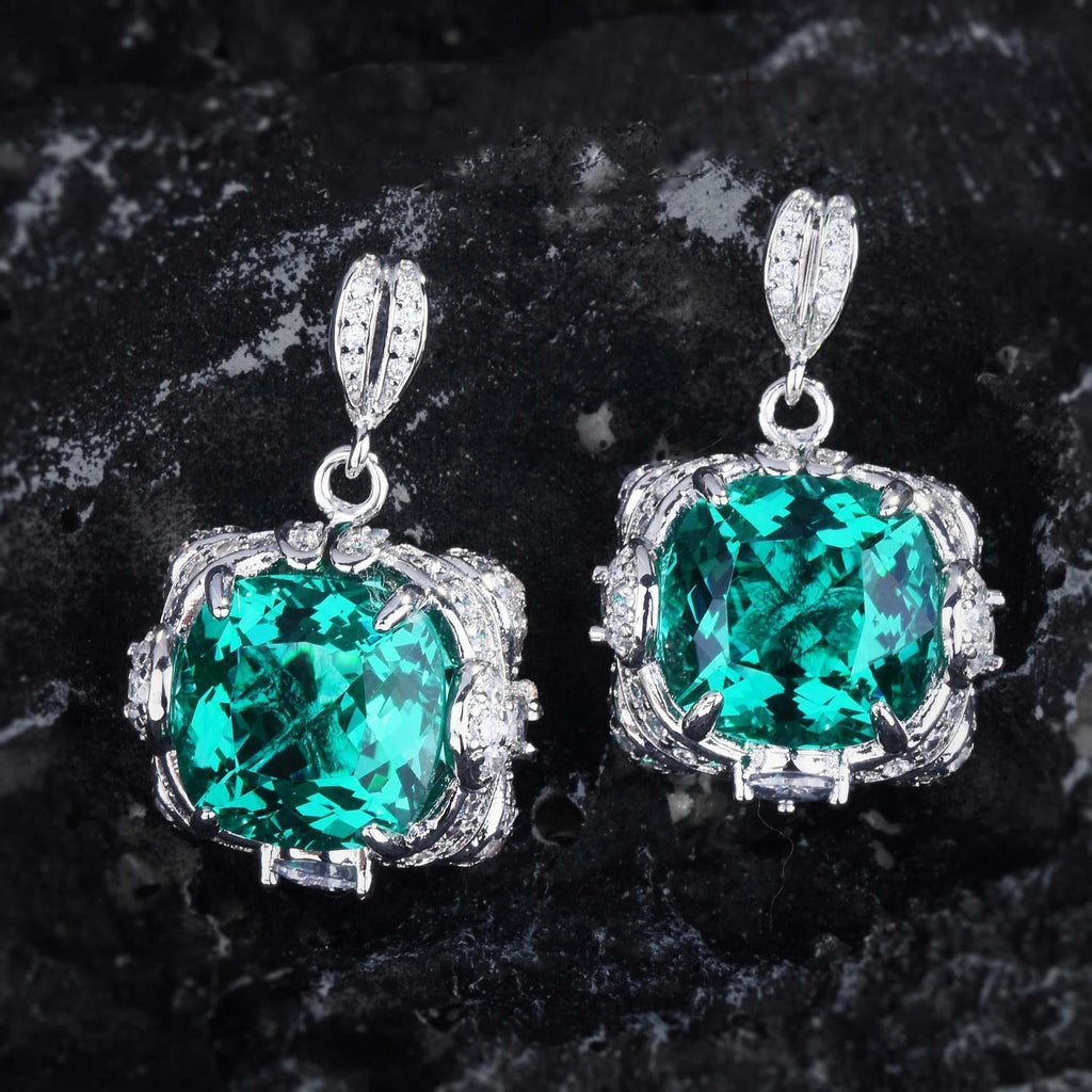 Pair of emerald green gemstone earrings with silver settings on a dark stone background