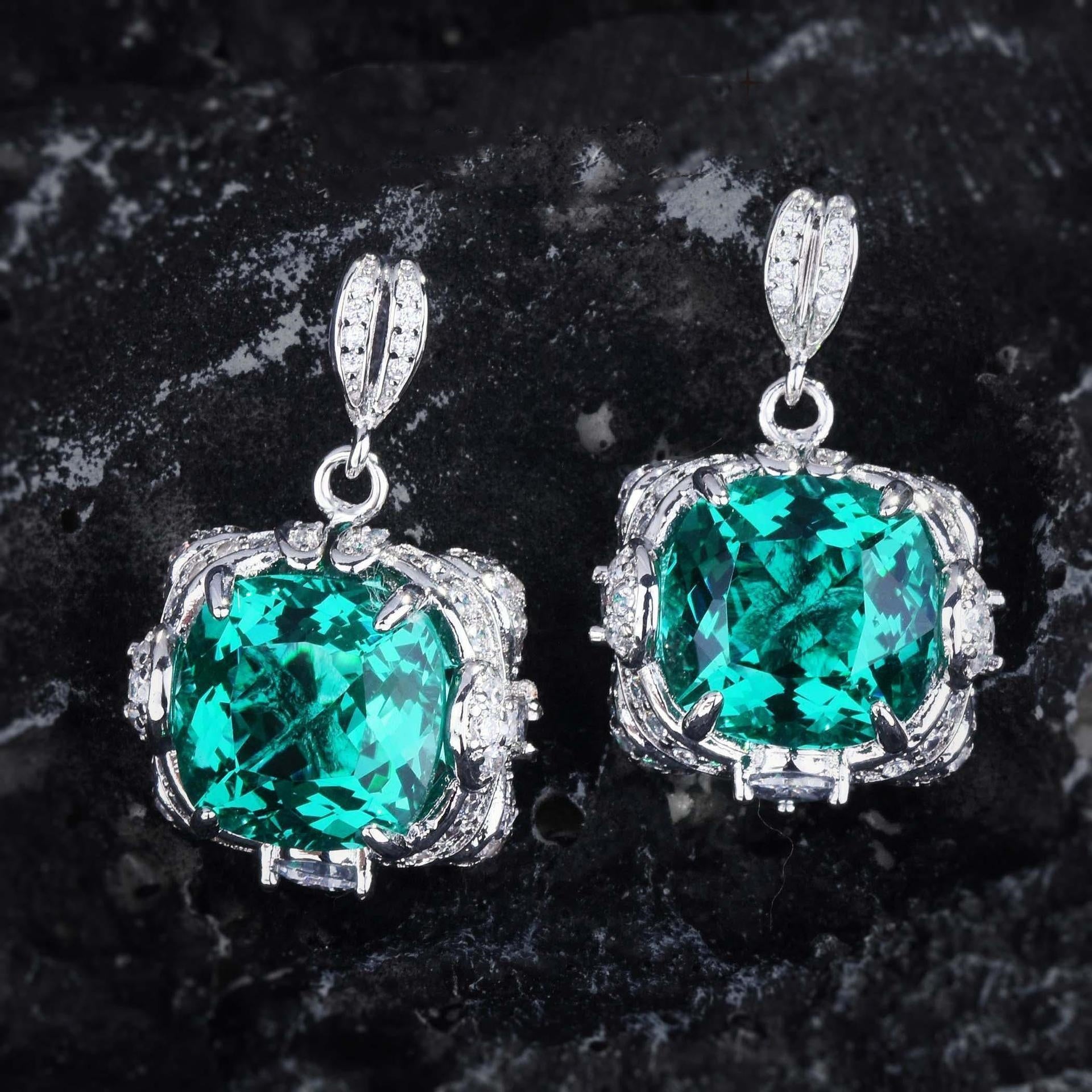 Pair of emerald green gemstone earrings with silver settings on a dark stone background