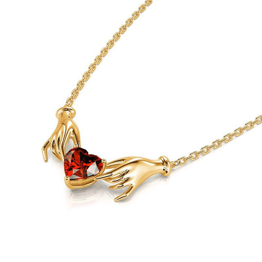 Gold necklace with a heart-shaped red gemstone held by two hands on a white background