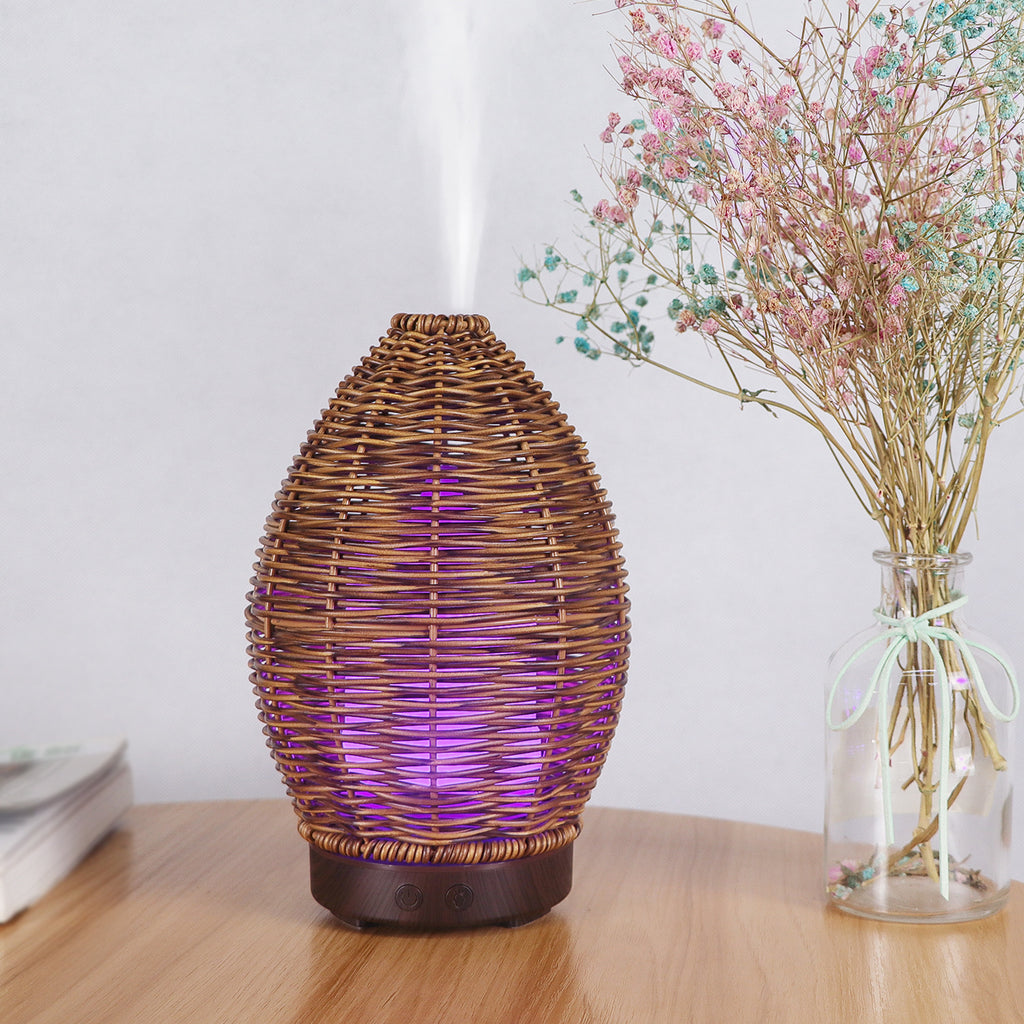 Wicker lamp with purple light on a wooden surface next to a vase with dried flowers.