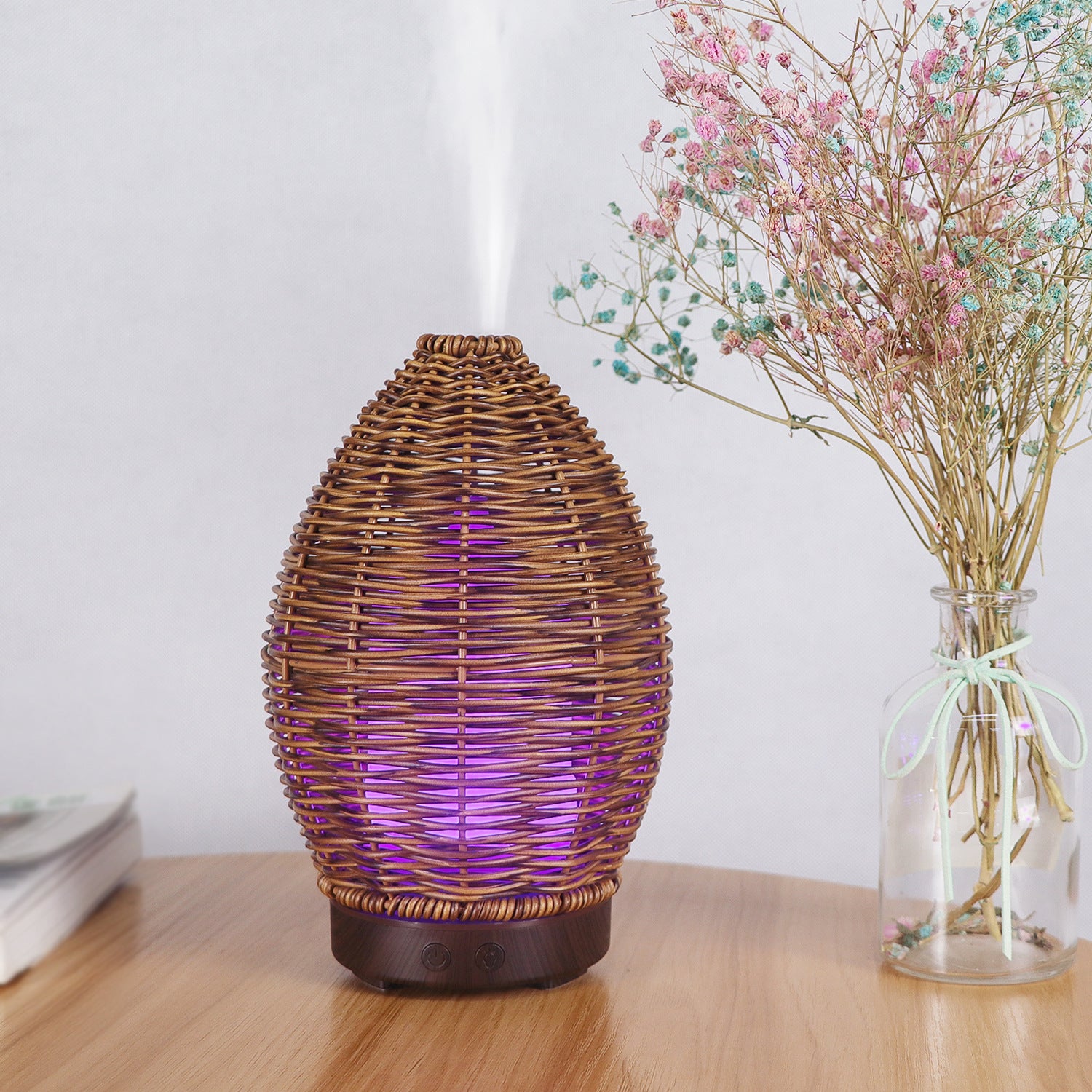 Wicker lamp with purple light on a wooden surface next to a vase with dried flowers.