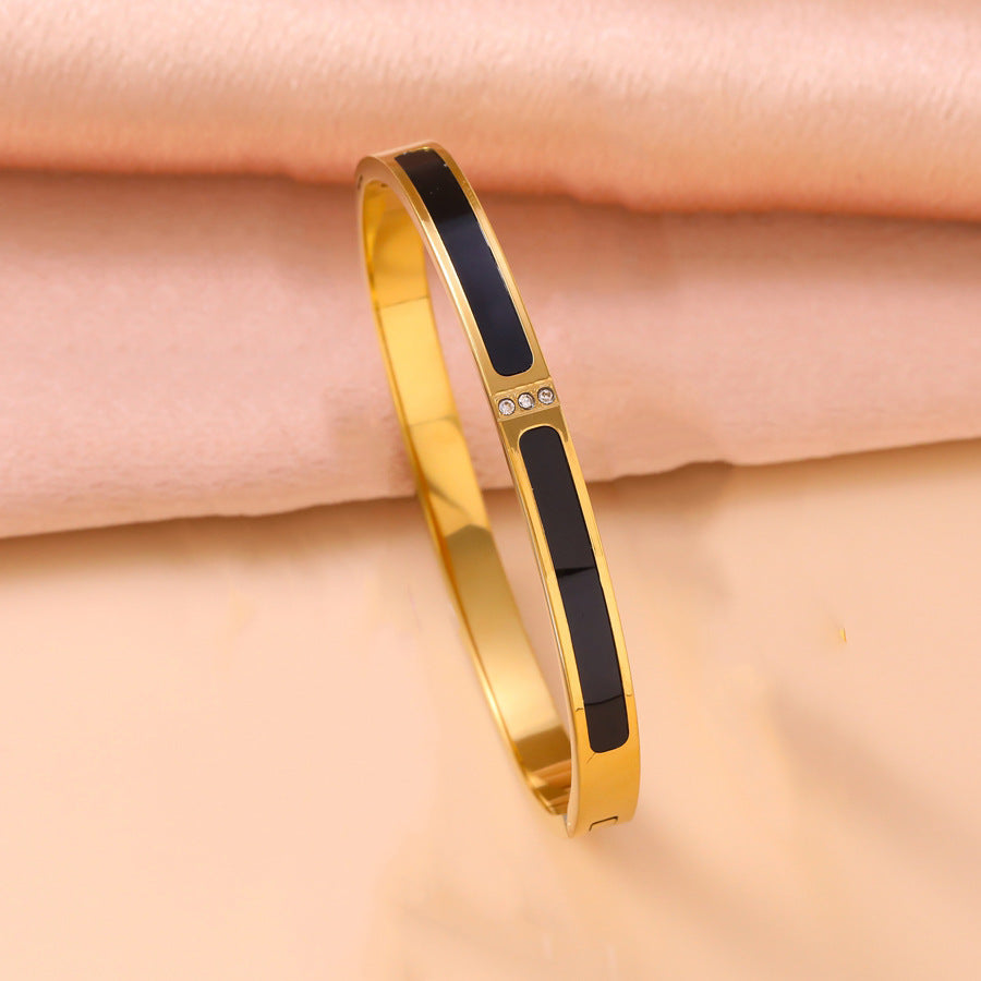 Gold bracelet with black accents on a pink fabric background