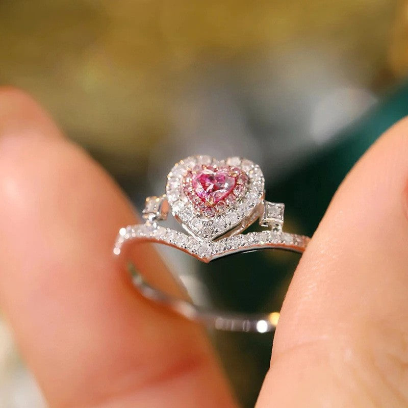Heart-shaped pink gemstone ring with diamond accents on a finger
