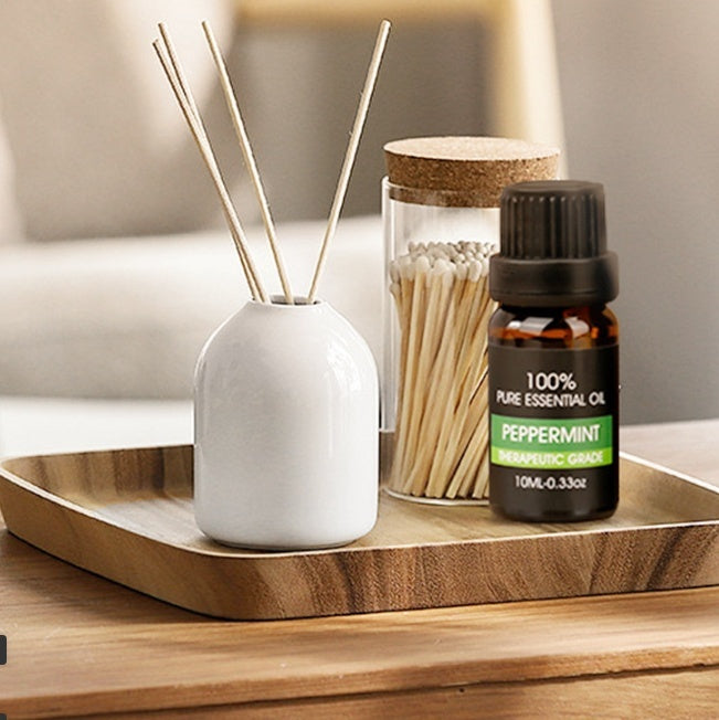 Peppermint essential oil bottle on a wooden tray with diffuser and matches.