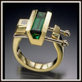 Gold ring with green gemstone and diamond on a dark background
