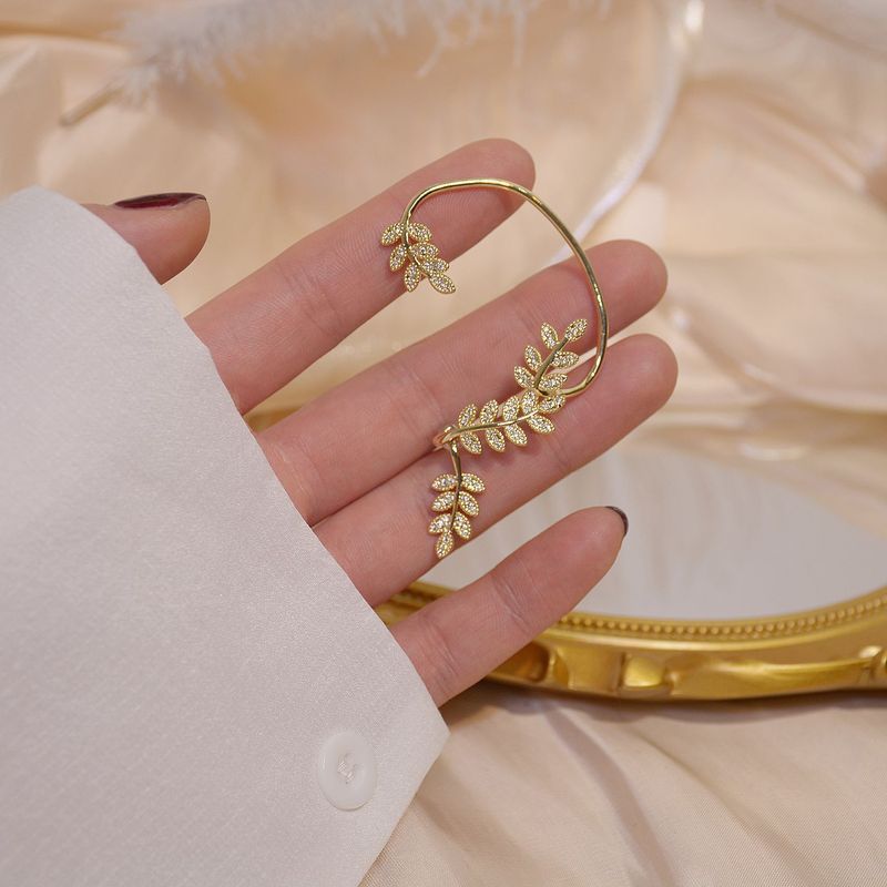 Gold leaf earrings being held by a hand with a soft background