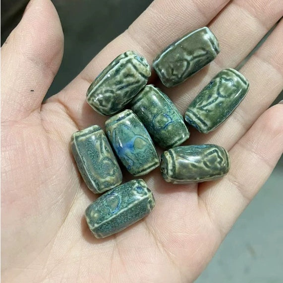 Hand holding several green ceramic beads with intricate designs.