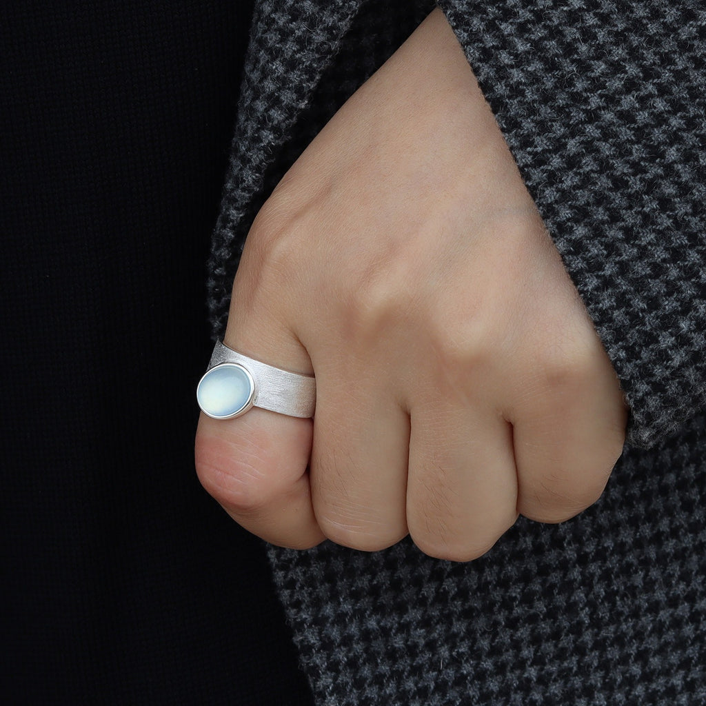 Hand wearing a silver ring with a dark background