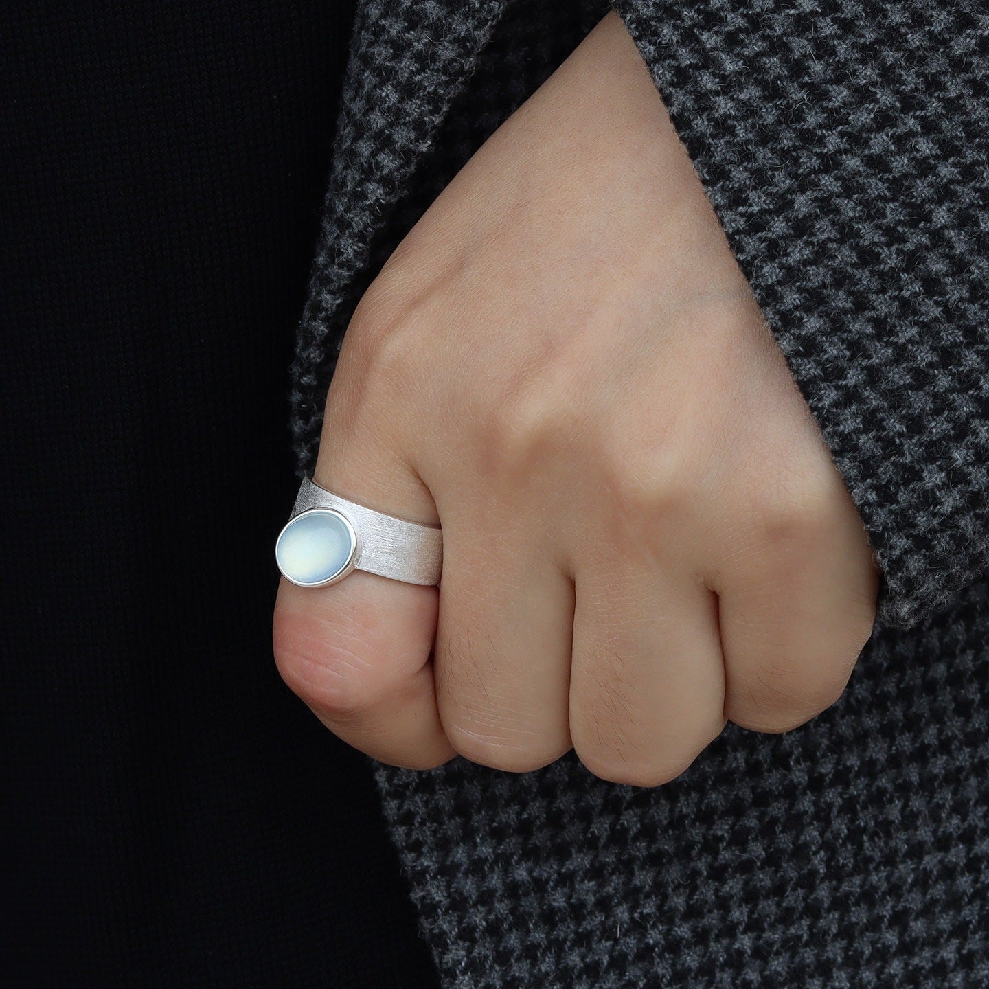 Hand wearing a silver ring with a dark background