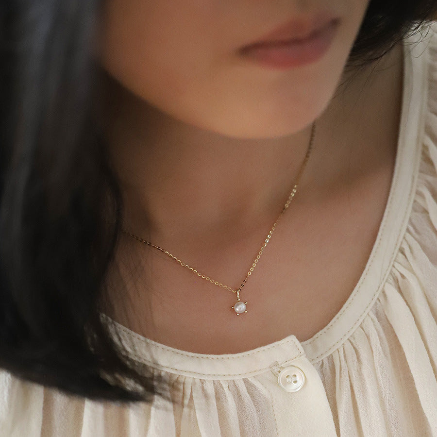 Close-up of a person wearing a delicate gold necklace with a small pendant.
